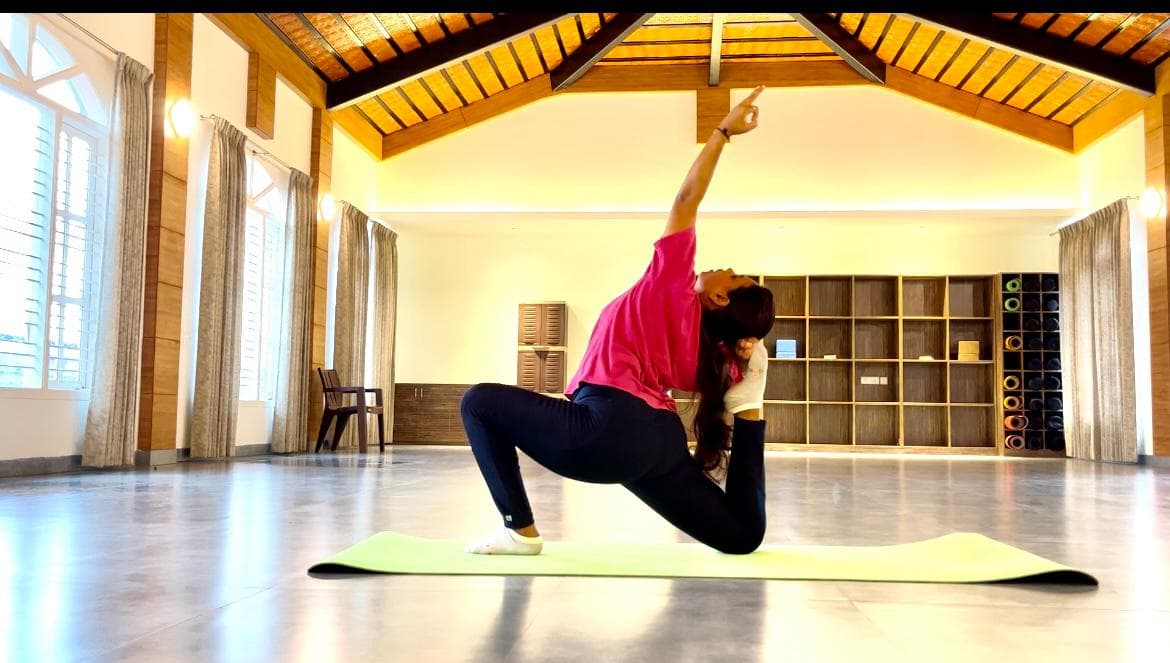Shiya Shahi in a lunge with one arm reaching up in a yoga hall
